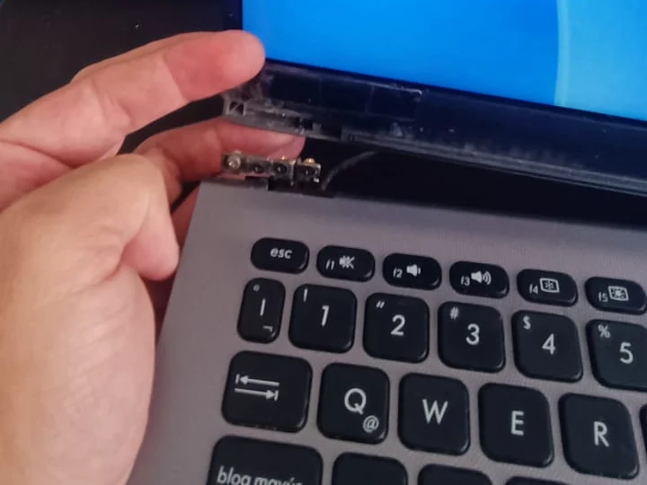 Técnico ajustando la bisagra de una laptop con la pantalla encendida en el taller